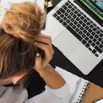 Stressed woman holding her head, staring down at her desk